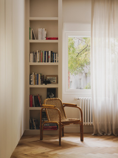 Rincón de lectura con librería, sillón de madera y ventana del proyecto AC55